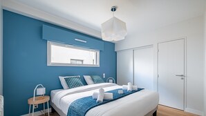 A modern bedroom with a large bed, a bedside table, a lamp, and a window. - Kerblue - Charmante maison à 3 km de la plage (Carnac)