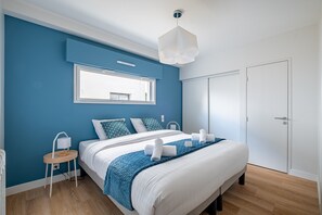 Ett modernt sovrum med en stor säng, ett sängbord, en lampa och ett fönster.