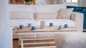 A white sofa with striped cushions, a wooden coffee table with blue cups, and a white ottoman. - Kerblue - Charmante maison à 3 km de la plage (Carnac)