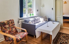 Una habitación acogedora con sofá, una silla estampada, una mesa y vistas por la ventana.