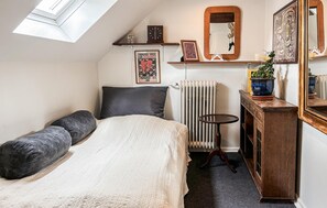 A bedroom with a bed, a radiator, a small table, a mirror, and wall decorations.