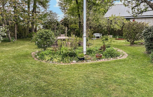A well-maintained garden with a central circular flower bed, a tall metal pole, and a white bench in the background.