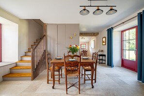 A dining area with a wooden table and chairs, a staircase, and a view through a window. - La Cidrerie - Havre de paix breton (Surzur)