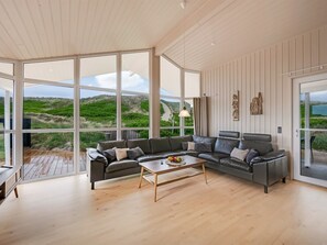 Ein geräumiges Wohnzimmer mit großem Fenster, einer Ledersofa, einem Holztisch und Blick ins Freie.