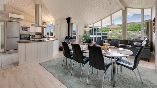 A modern kitchen with a built-in oven, a large island with seating, and a dining area with a round table and chairs. - "Mine" -  from the sea by Interhome (Hvide Sande)