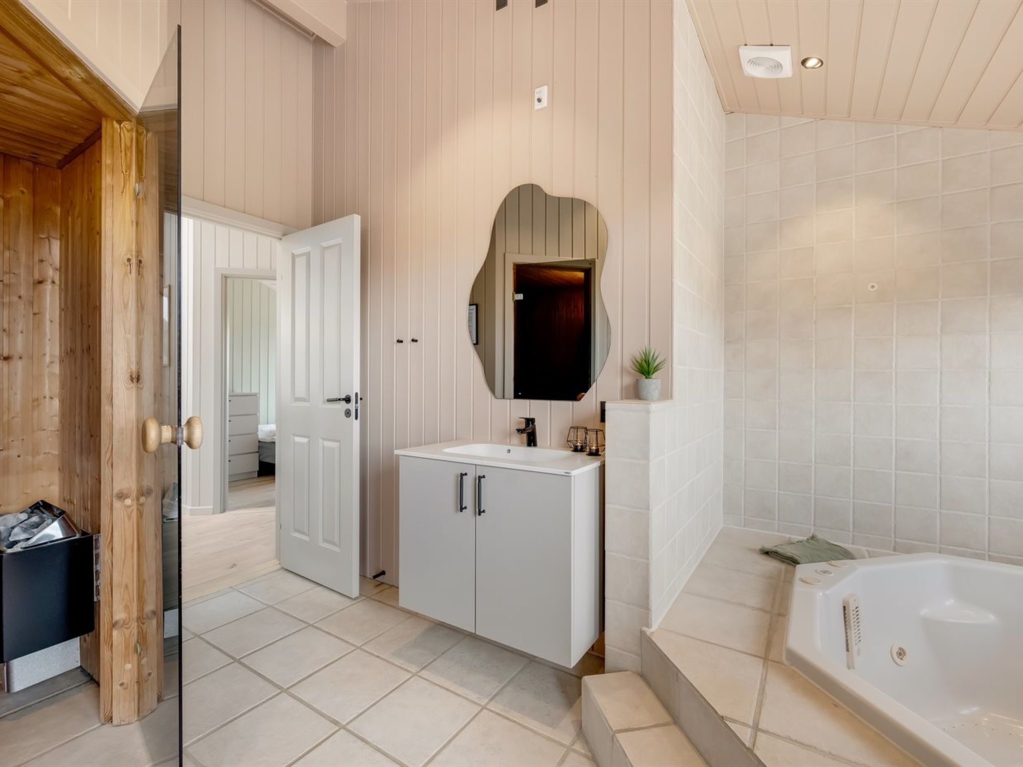 Une salle de bain moderne avec une grande baignoire, un meuble-lavabo avec un miroir et une porte donnant sur une autre pièce.