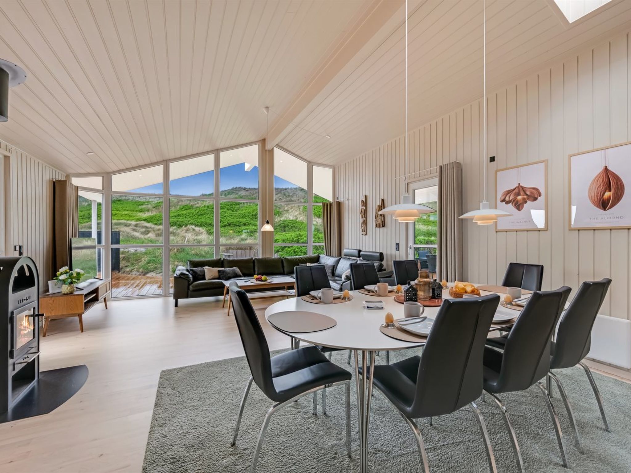Een modern interieur met een eethoek, bank en grote ramen met uitzicht op het omliggende landschap.
