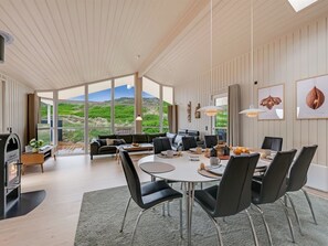 Ein modernes Interieur mit Essbereich, Sofa und großen Fenstern mit Blick ins Freie.