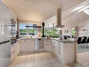 Eine moderne Küche mit einer großen Kochinsel, weißen Schränken und Blick ins Freie.