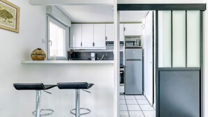 A modern kitchen with white cabinets, a stainless steel refrigerator, and a bar stool area. - Le Saint-Denis Pleyel - À 10 min de Paris en métro (Saint Denis)