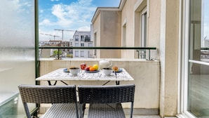 A balcony with a table set for two, two wicker chairs, and a view of buildings and a crane in the background. - Le Saint-Denis Pleyel - À 10 min de Paris en métro (Saint Denis)