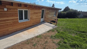 Una cabaña de madera con dos ventanas, una puerta y un camino de concreto que lleva a una terraza de madera.