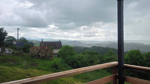Paisaje rural con una casa, una cerca de madera y vistas a colinas distantes.