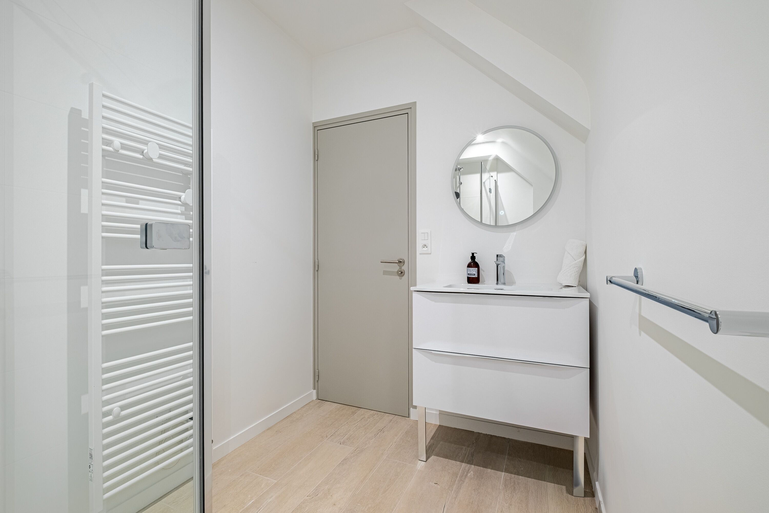 A modern bathroom with a white vanity, a round mirror, and a glass shower enclosure.