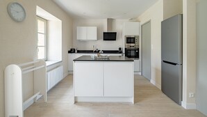 Eine moderne Küche mit weißen Schränken, einer zentralen Kochinsel, einem eingebauten Backofen und einem Kühlschrank.