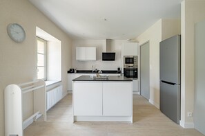 A modern kitchen with white cabinetry, a central island, a built-in oven, and a refrigerator. - Longère Kerlescan - À 5 km de la plage (Carnac)