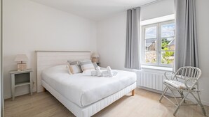 Ein Schlafzimmer mit Bett, Nachttischen, einem Sessel, einem Fenster mit Vorhängen und Blick ins Freie.