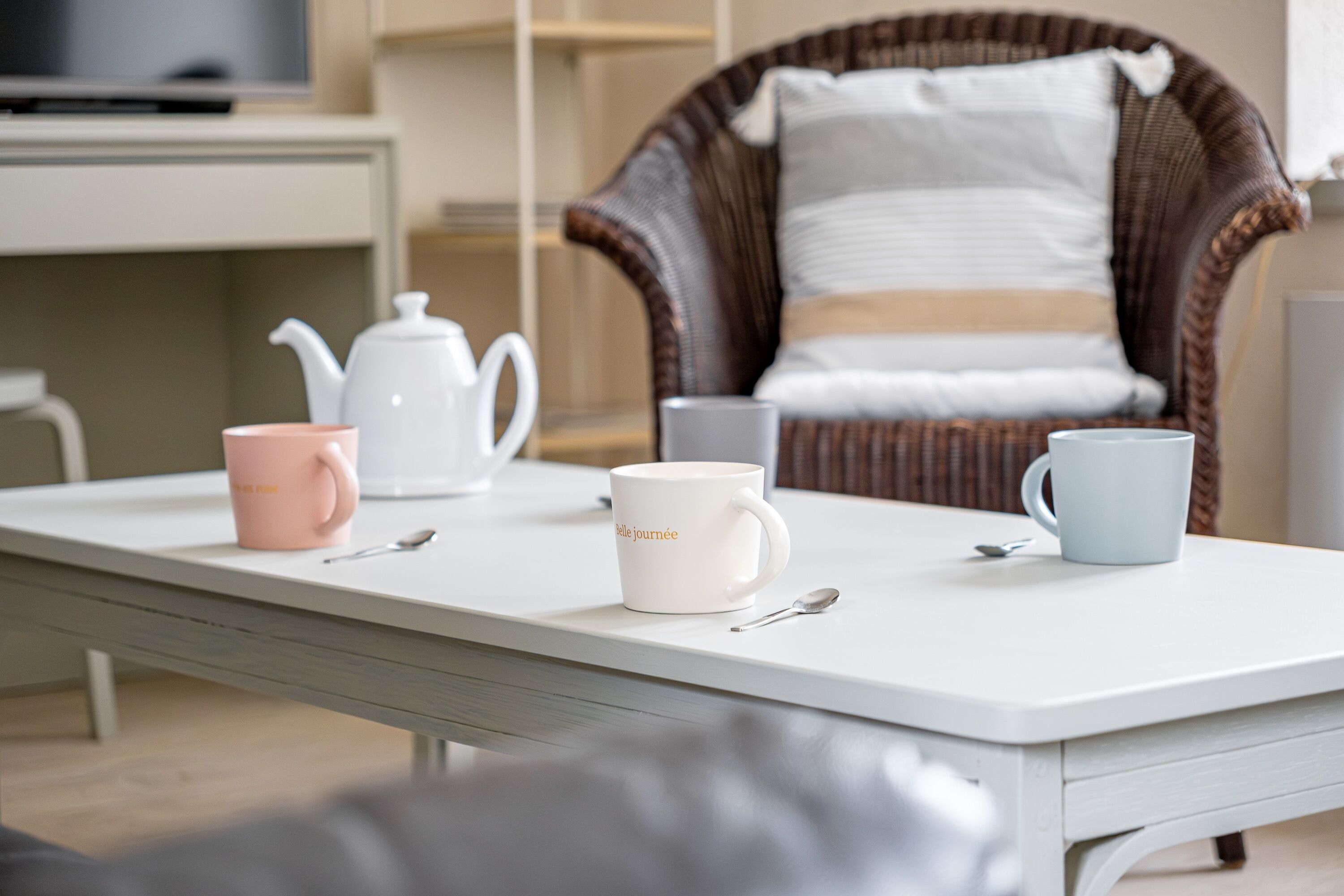 A white table with three mugs, a teapot, and a spoon.