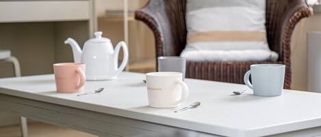 A white table with three mugs, a teapot, and a spoon.