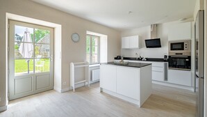 Eine moderne Küche mit weißen Schränken, einer zentralen Kochinsel, einem eingebauten Backofen, einer Mikrowelle und einem Flachbildfernseher.