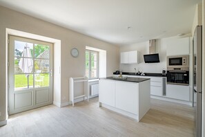 A modern kitchen with white cabinetry, a central island, a built-in oven, microwave, and a flat-screen TV. - Longère Kerlescan - À 5 km de la plage (Carnac)