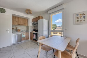 Eine moderne Küche mit Holzausstattung, einem weißen Kühlschrank, einem Esstisch mit Stühlen und einem Fenster mit Blick auf die Stadt.