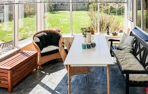 Ein Wintergarten mit Korbmöbeln, einem weißen Tisch und Blick auf einen Garten.