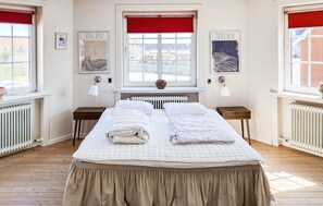Ein Schlafzimmer mit einem Bett, zwei Nachttischen, einem Fenster mit rotem Rollo und einer Heizung.