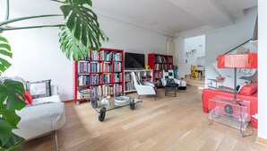 A modern living room with a sofa, a glass coffee table, a bookshelf, a TV, and a red couch. - Atelier des Harmonies - L'atelier d'artiste au cœur de Lyon (Lyon)