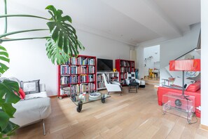 A modern living room with a sofa, a glass coffee table, a bookshelf, a TV, and a red couch. - Atelier des Harmonies - L'atelier d'artiste au cœur de Lyon (Lyon)