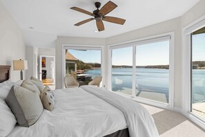 Ein Schlafzimmer mit einem großen Bett, einem Deckenventilator und Blick auf ein Gewässer durch große Fenster.