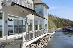 Ein Anwesen am Wasserufer, mit Balkon, großen Fenstern und Blick auf das Wasser.