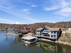 Ein großes Haus mit Steg und Kleinboot, umgeben von einem See und Bäumen.