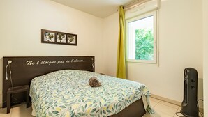 Quarto com cama, mesa de cabeceira, janela com cortinas, um quadro pendurado na parede e um aquecedor.