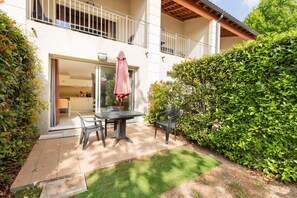 A two-story building with a balcony, a patio with a table and chairs, and a well-maintained hedge. - Casa Jouarres - Appartement avec terrasse privée (Azille)