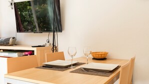Uma área de refeições com uma mesa posta para dois, uma TV de tela plana na parede e um relógio também na parede.