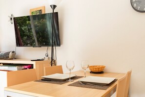 A dining area with a table set for two, a flat-screen TV mounted on the wall, and a clock on the wall. - Casa Jouarres - Appartement avec terrasse privée (Azille)
