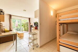 A room with a bunk bed, a desk, a chair, a small table, a cart, and a window with a view of greenery. - Casa Jouarres - Appartement avec terrasse privée (Azille)