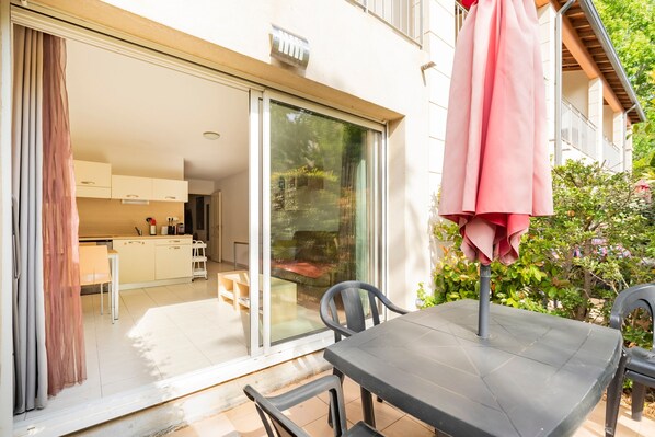 A patio with a table and chairs, a sliding glass door leading to a kitchen, and a balcony with a pink umbrella. - Casa Jouarres - Appartement avec terrasse privée (Azille)