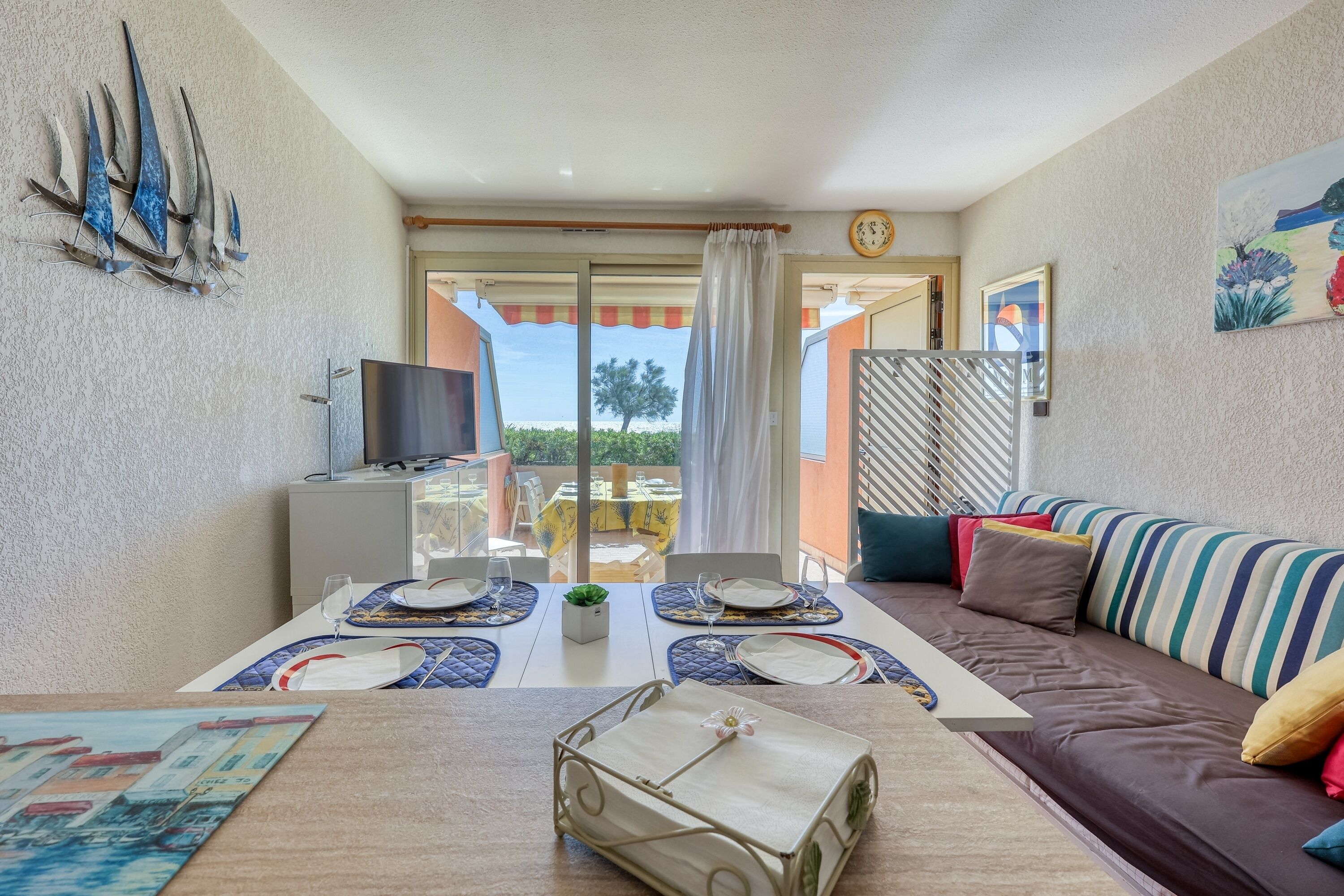 Ein Essbereich mit Tisch für zwei Personen, einer Couch, einem Fernseher und Blick ins Freie.