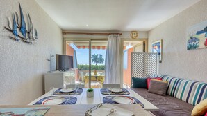 A dining area with a table set for two, a sofa, a TV, and a view of the outdoors. - L’Orée des Sables - Vue mer & plage à 15 m (Le Lavandou)
