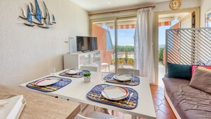 A dining area with a table set for two, a TV, and a balcony with a view. - L’Orée des Sables - Vue mer & plage à 15 m (Le Lavandou)