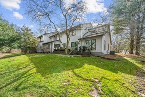 A two-story house with a front porch, a well-maintained lawn, and trees in the background. - Irish Family Villa! Close to ND! (Granger)