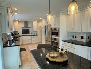 A modern kitchen with white cabinetry, a black countertop, and a central island with a vase and decorative bowl. - Irish Family Villa! Close to ND! (Granger)