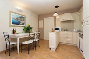 Una cocina compacta con muebles blancos, una mesa de comedor con sillas, una lámpara colgante y un cuadro en la pared.