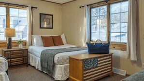A bedroom with a bed, a nightstand, a lamp, a window with curtains, and a dresser with an American flag design. - Mountainview - Guest House by Avantstay Heated Pool + Hot Tub + Games Lake + Cannoe Near Hunter Mountain (Hensonville)