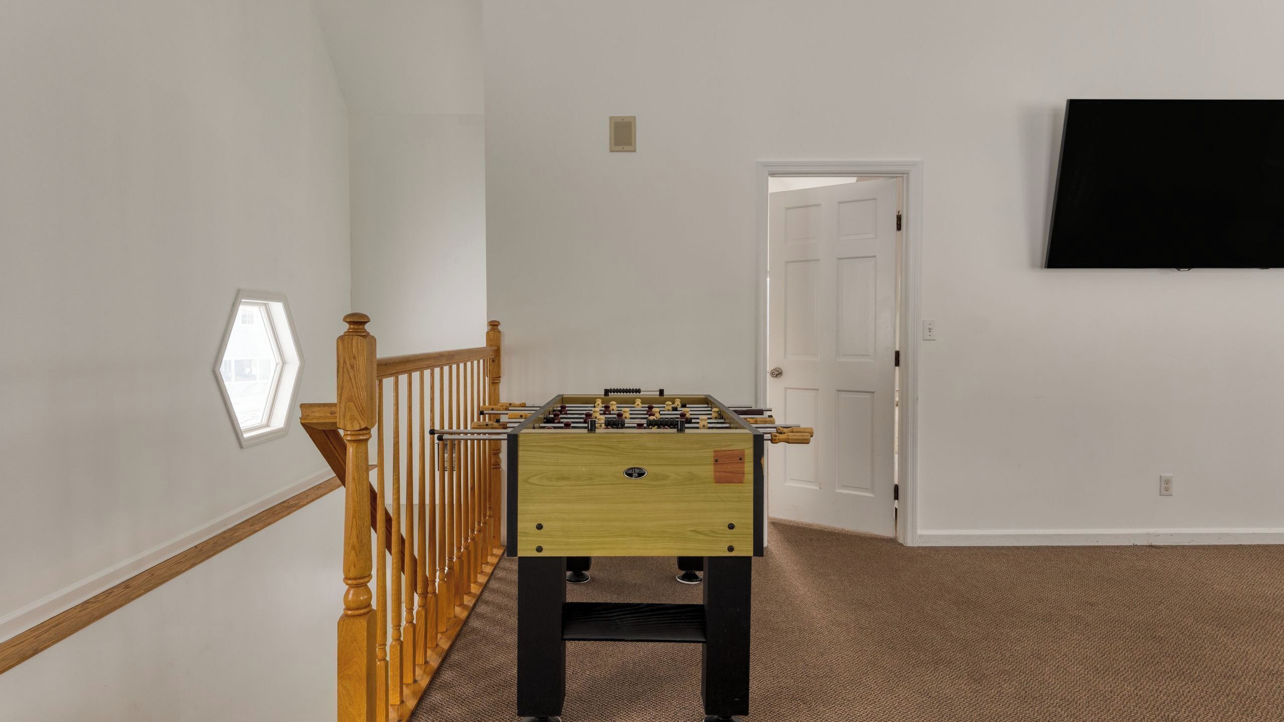 A room with a wooden foosball table, a white door, and a mounted television on the wall.