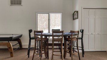 A room with a pool table, four wooden chairs, a table with a blue surface, and a white door.