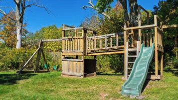 Une structure de jeux en bois comprenant un toboggan, des balançoires et des éléments d’escalade.