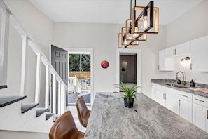 A modern kitchen with a marble countertop, white cabinets, and a unique pendant light.